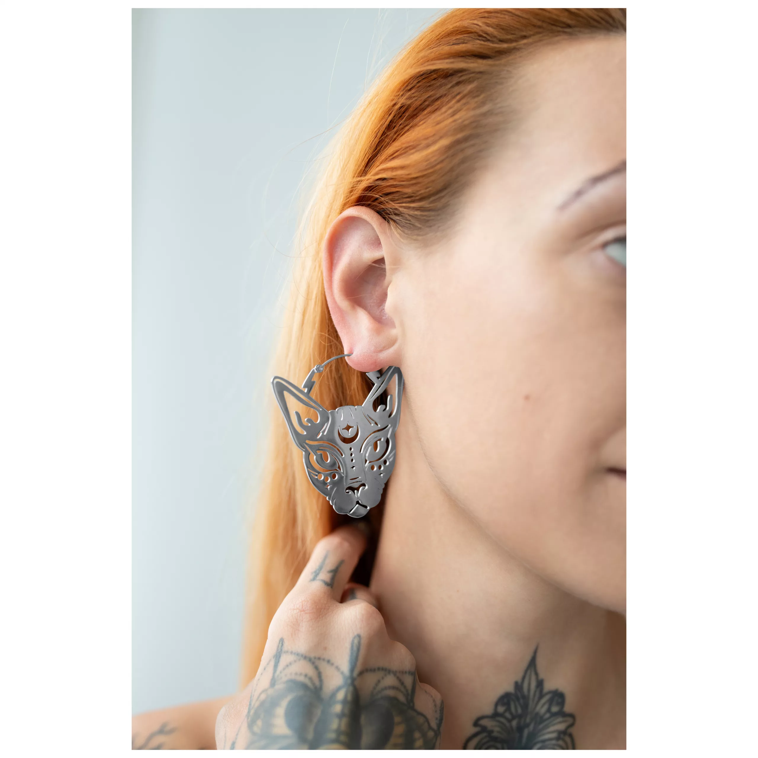 Sphynx Hoops Ohrringe aus Chirurgenstahl Silberne Sphynx Hoops Ohrringe an einem Ohr mit tätowierter Hand