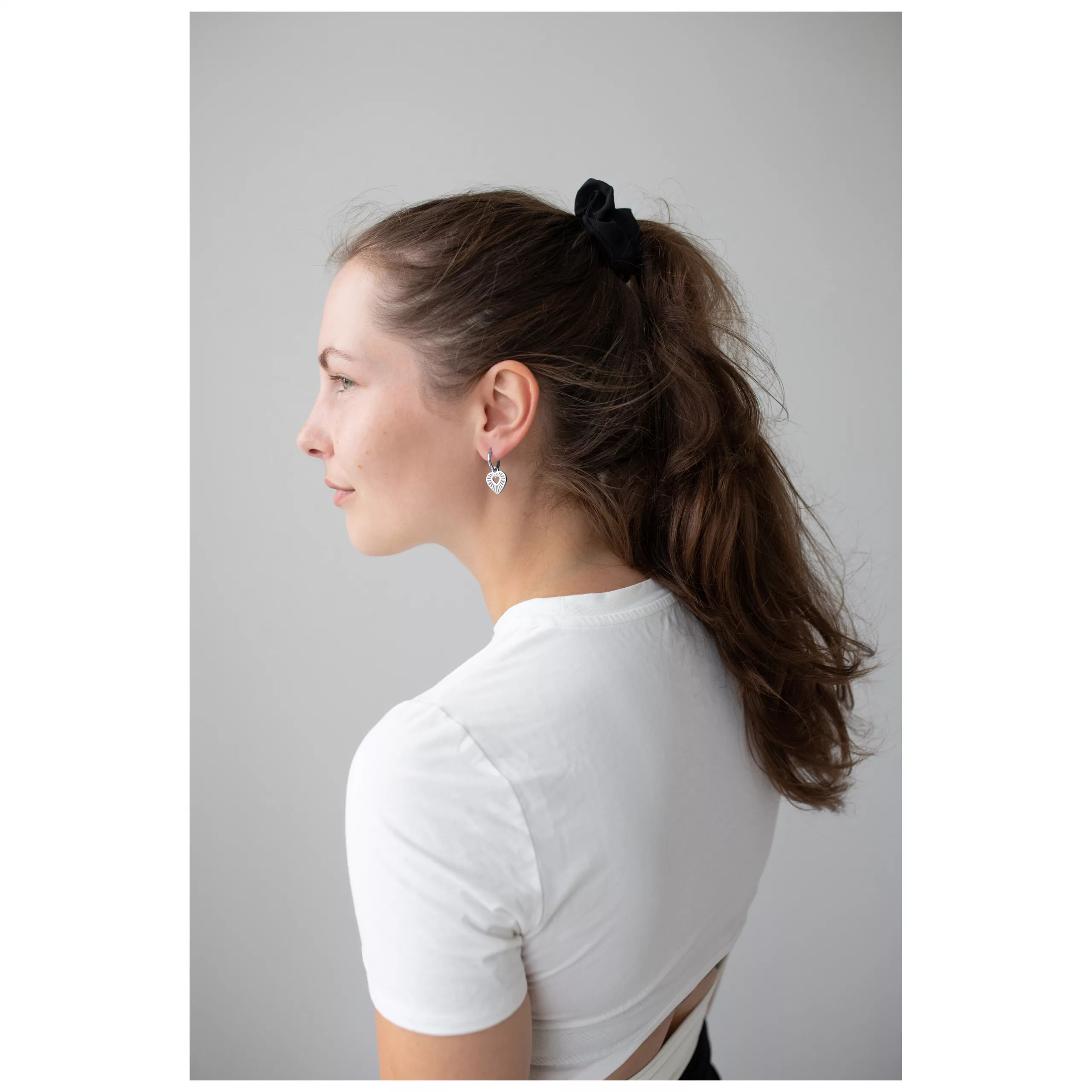 Elegante Herz Creolen in Silber Frau mit weißen T-Shirt trägt silberne Herz Creolen vor grauem Hintergrund
