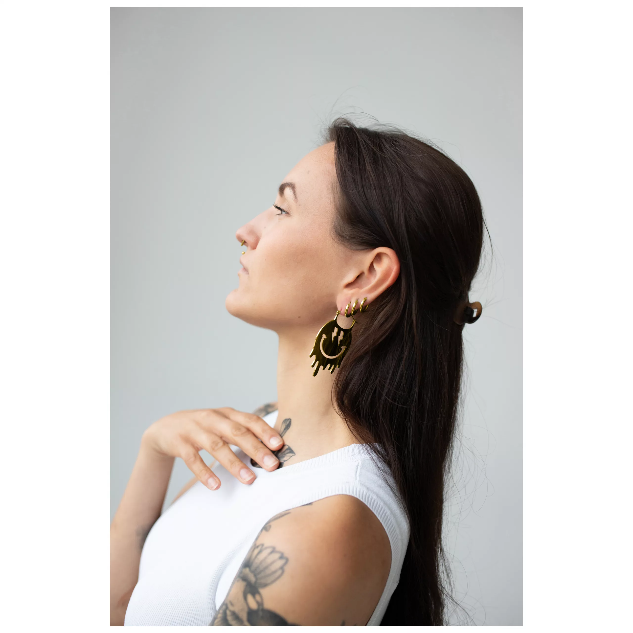 Smiley Big Hoops Pairs in Gold am Ohr Frau mit langen Haaren trägt goldene Smiley Ohrringe auf grauem Hintergrund
