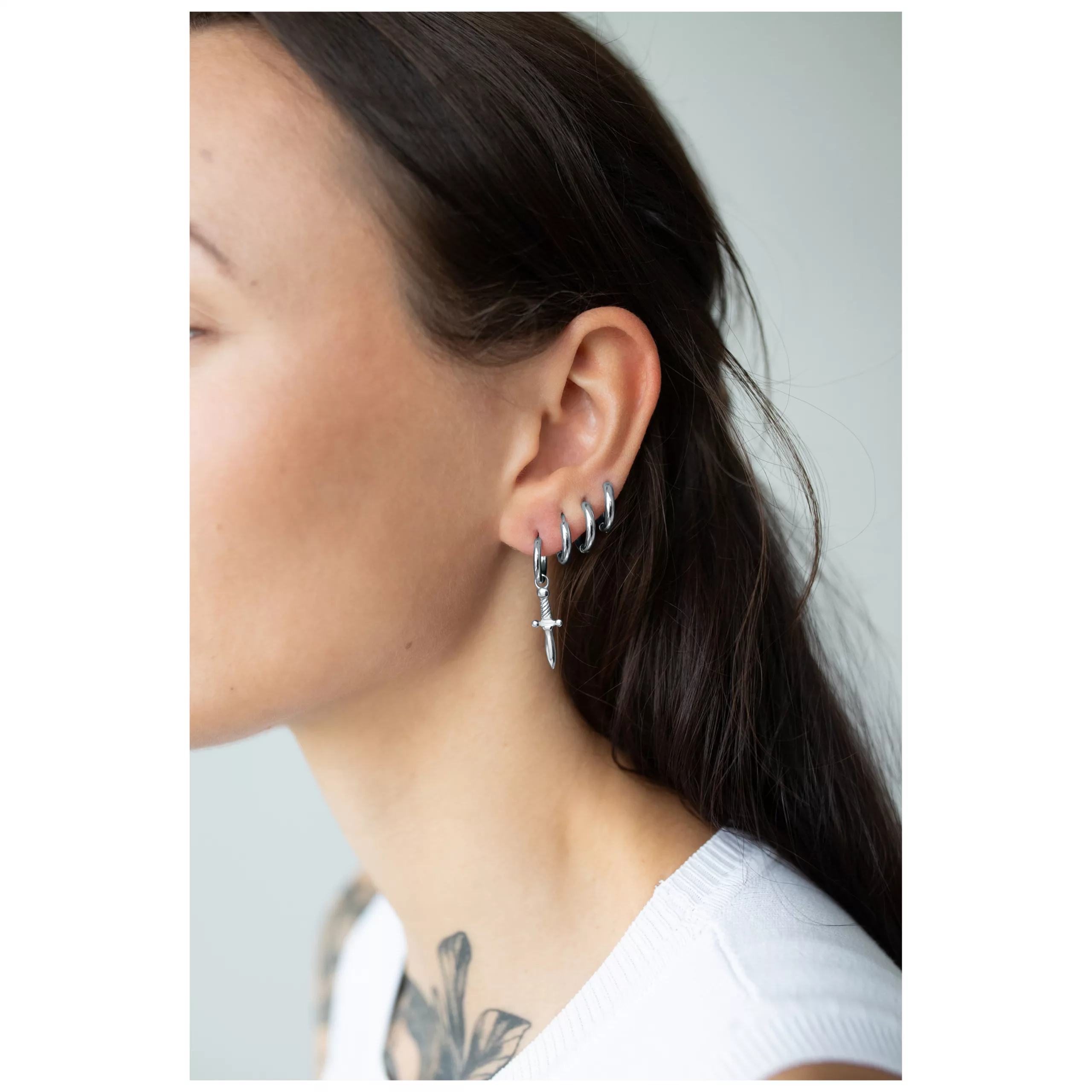 Elegante Little Sword Hoops in Silber Silberne Ohrringe in Schwertform an weiblichem Ohr auf neutralem Hintergrund
