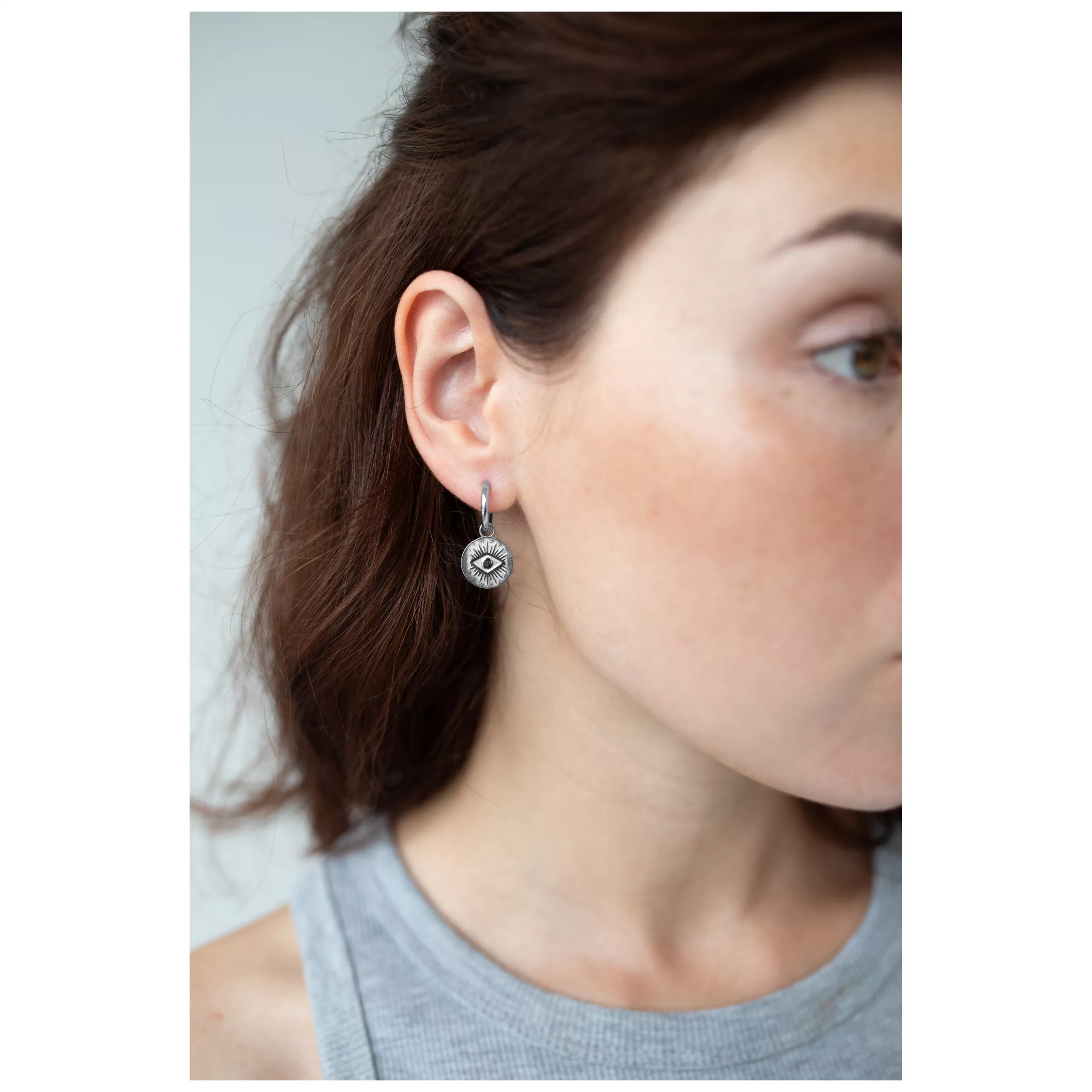 Silberne Little Luminous Eye Hoops Ohrringe Frau trägt silberne Ohrringe mit Augenmotiv, seitliche Ansicht