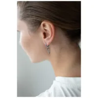 Schwarze und silberne Dreieck Creolen am Ohr einer Person mit braunem Haar, weißer Hintergrund