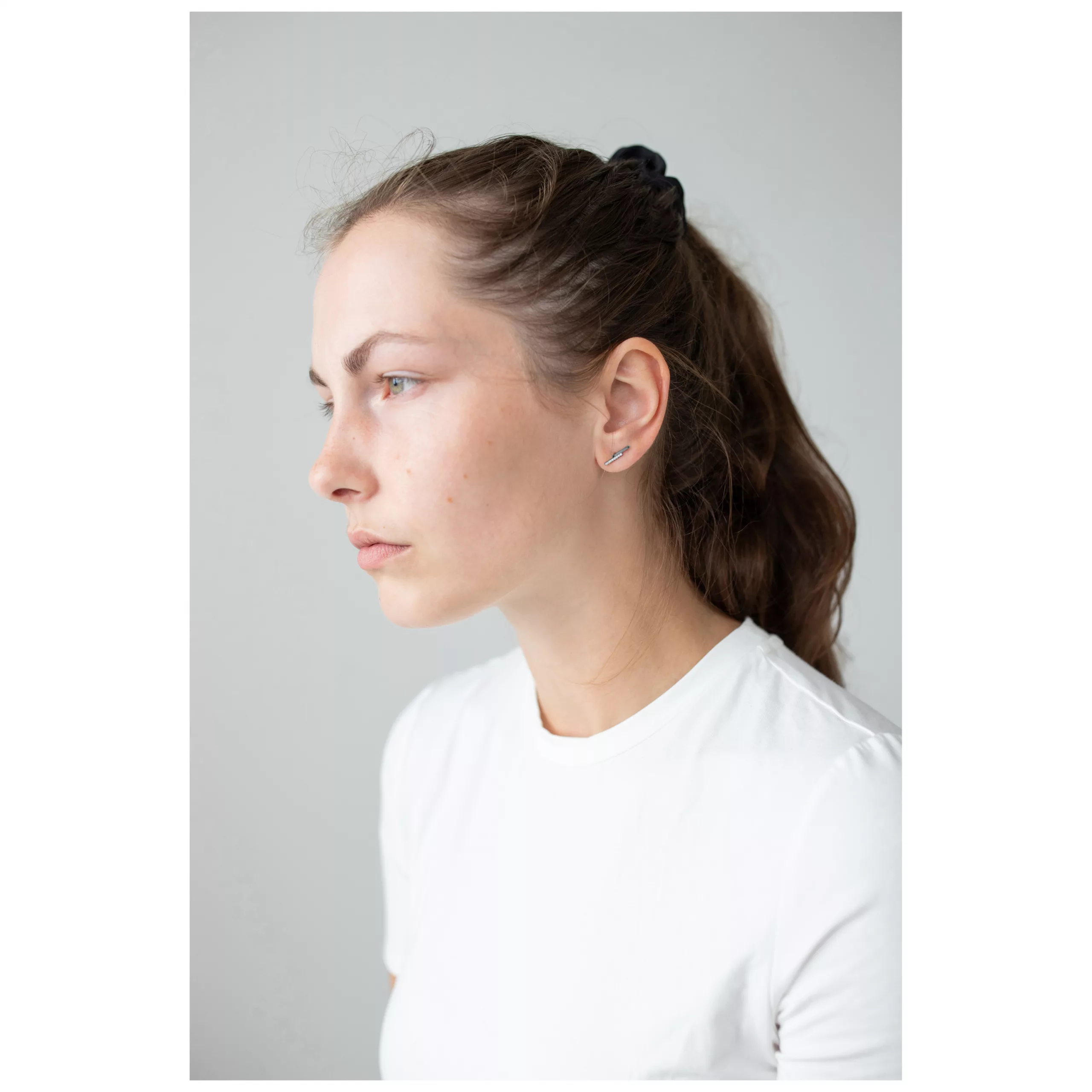 Elegante Ohrstecker aus Edelstahl Frau mit braunem Haar trägt dezente, silberne Ohrstecker vor grauem Hintergrund