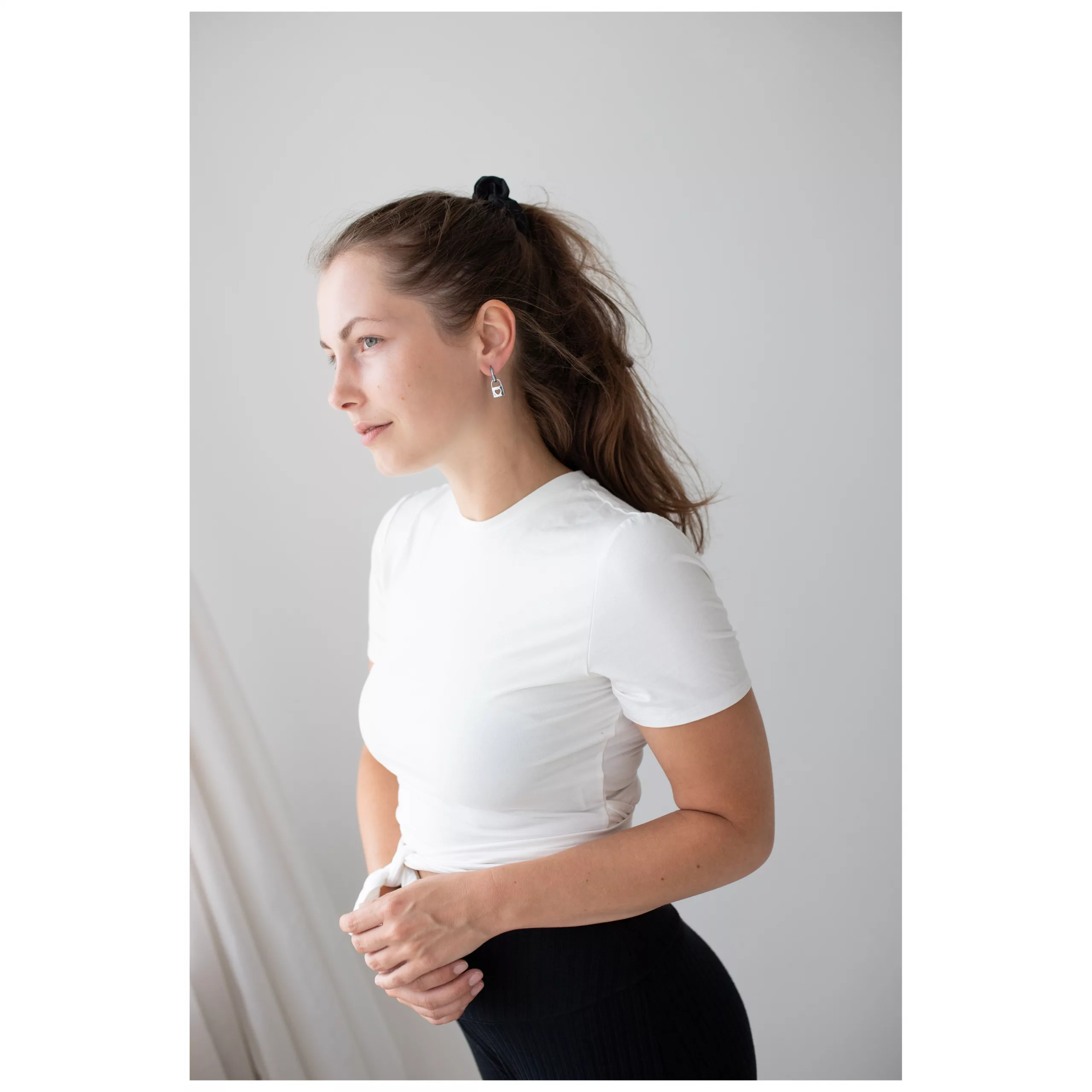 Frau mit weißen T-Shirt und eleganten silbernen Ohrringen vor neutralem Hintergrund