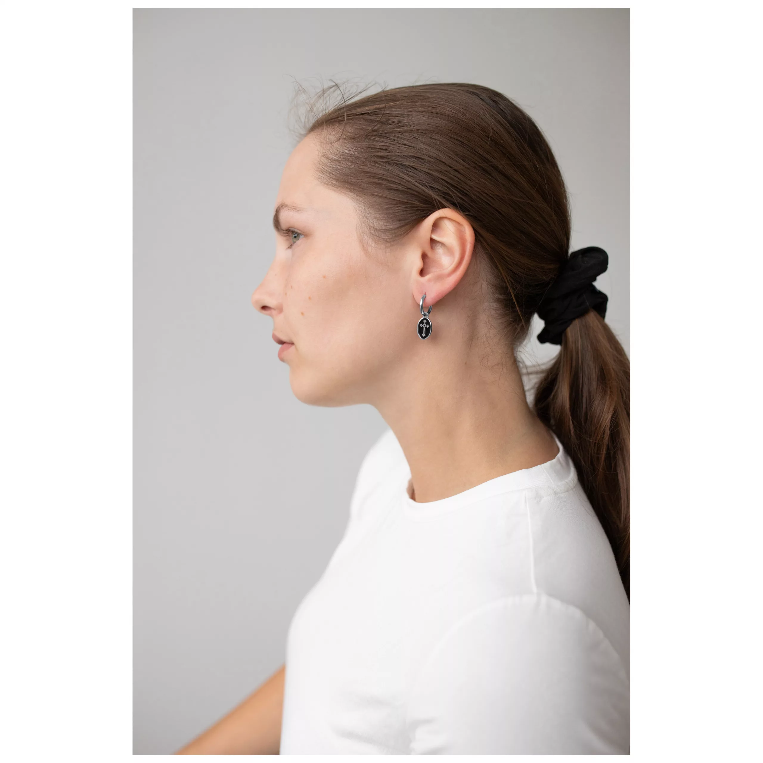 Elegante Vintage Kreuz Creolen in Silber Frau mit langen Haaren trägt silberne Kreuz Creolen vor grauem Hintergrund