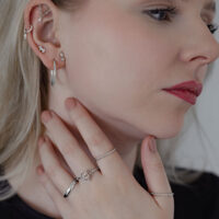 Eleganter Twisted Ring in Silber getragen Frau mit mehreren Ohrringen, die einen silbernen Twisted Ring trägt