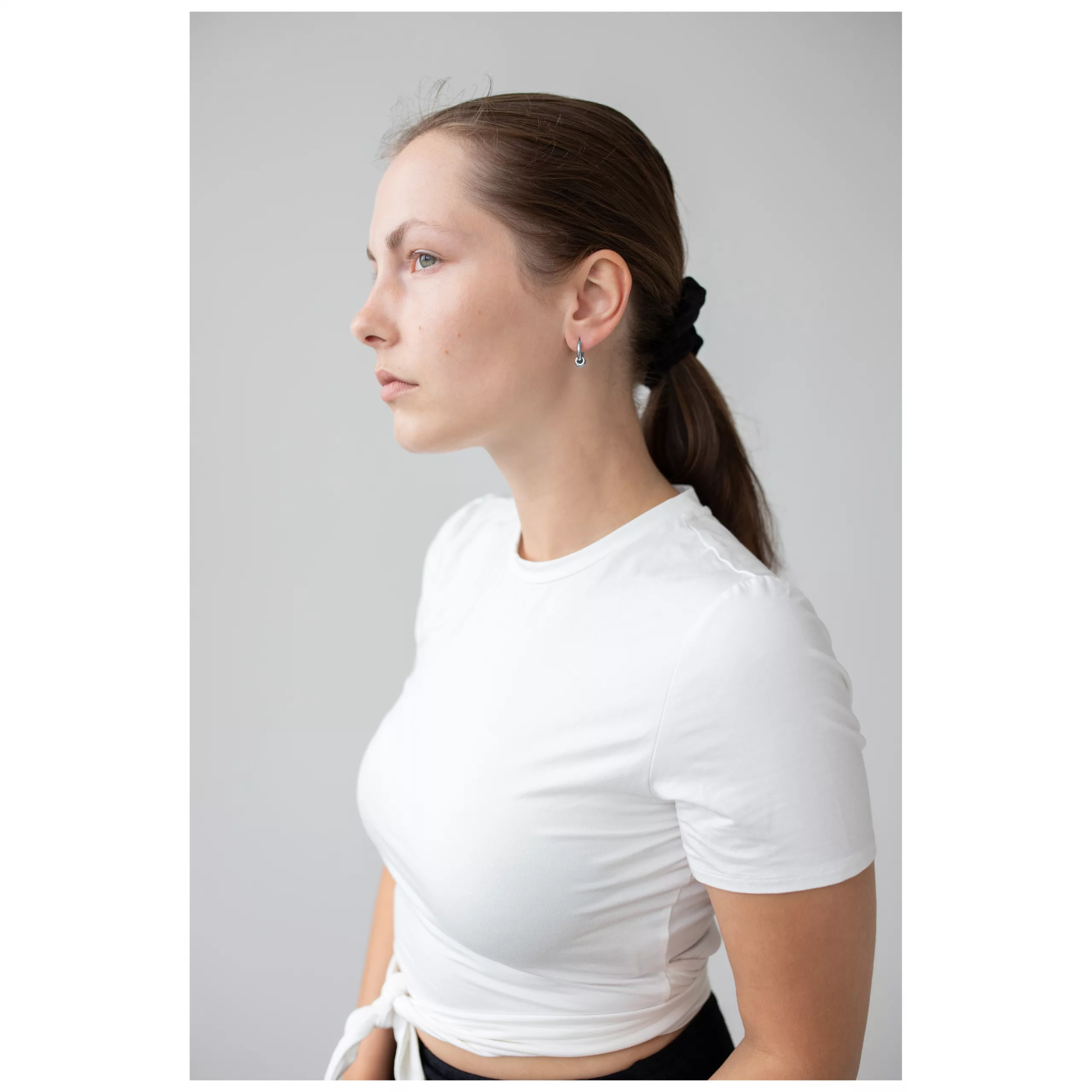 Frau mit Little 5 Rings Hoops Ohrringen in Schwarz und Silber vor grauem Hintergrund