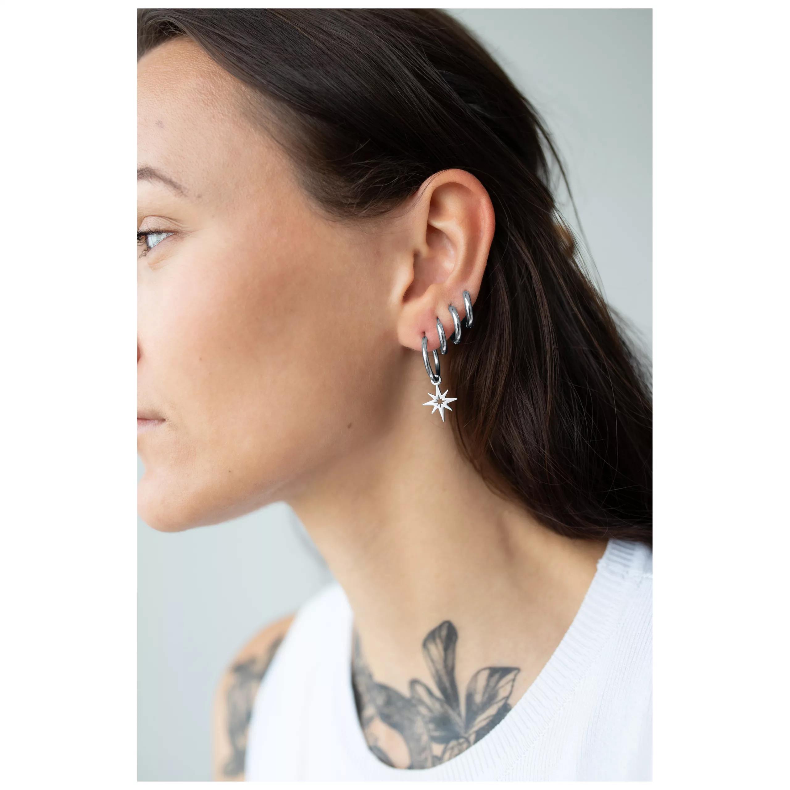 Silberne Little Polar Star Hoops im Ohr Frau trägt silberne Ohrringe mit Sternanhänger auf weißem Hintergrund