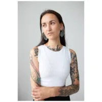Frau mit tätowierten Armen trägt Monstera Leaf Hoops Ohrringe, weißes Top