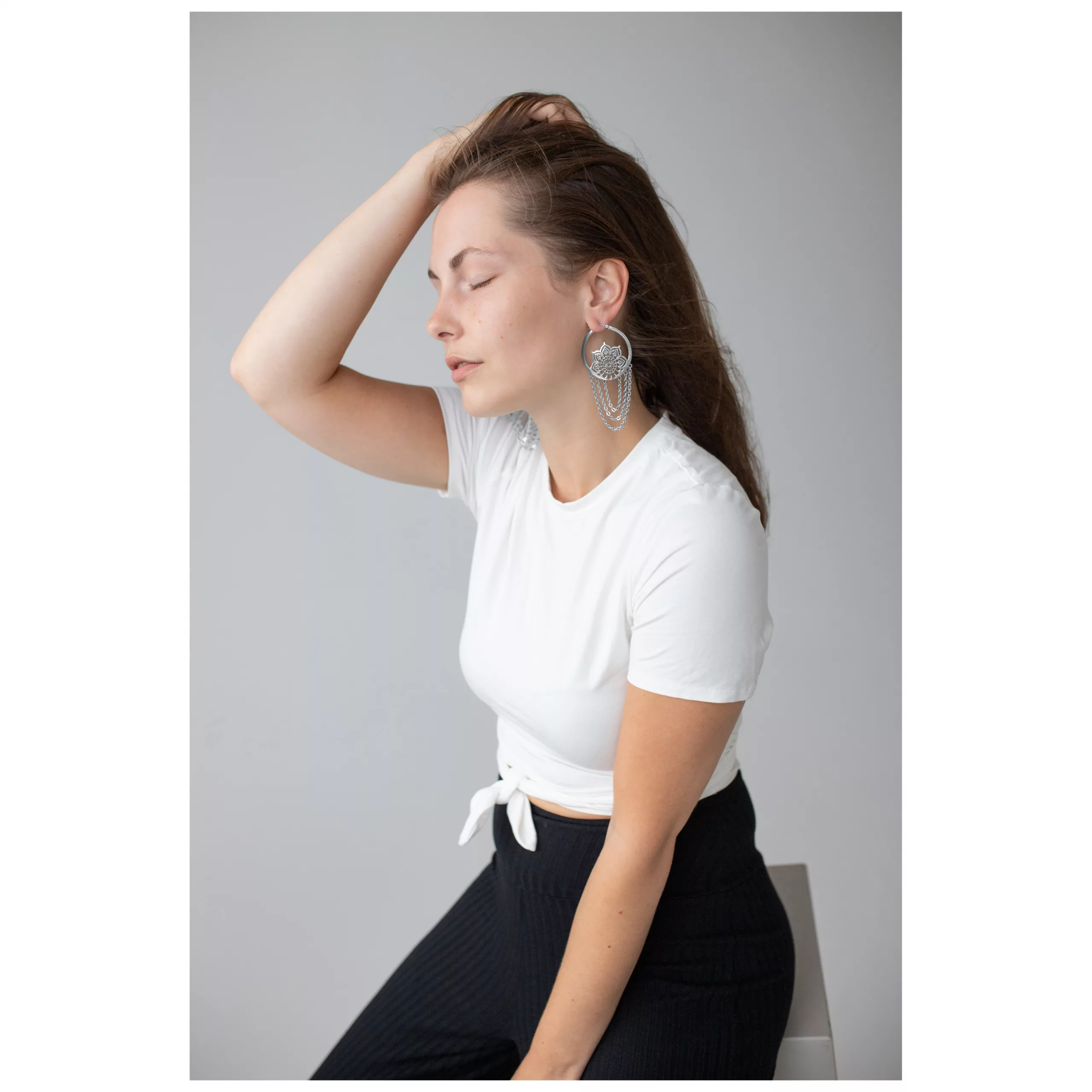 Elegante La Fleur Hoops in Silber Frau mit weißen T-Shirt trägt elegante silberne La Fleur Ohrringe auf grauem Hintergrund