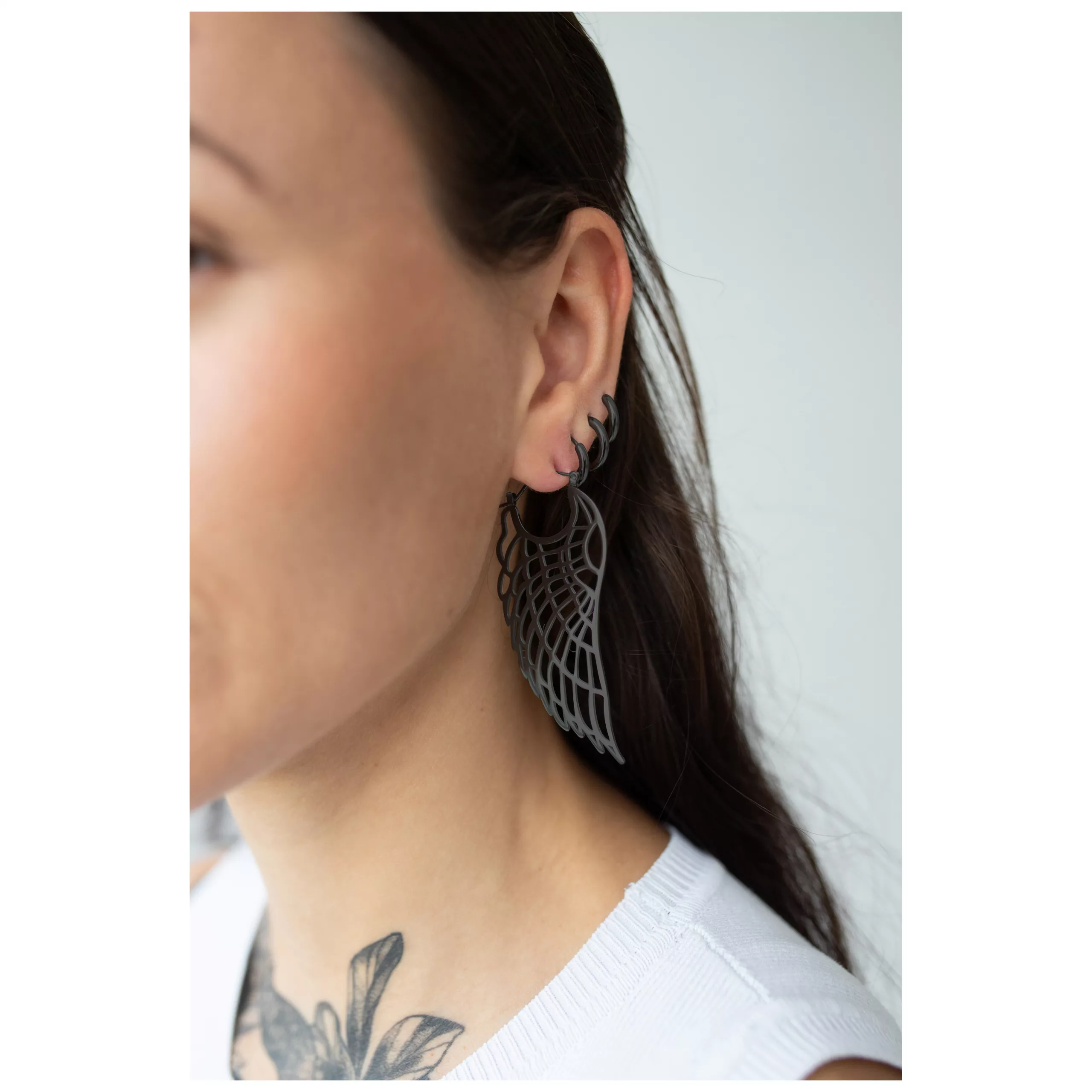 Elegante Wing Hoops Ohrringe in Schwarz Nahaufnahme von schwarzen Wing Hoops Ohrringen an einem Ohr, getragen von einer Person mit langen dunklen Haaren