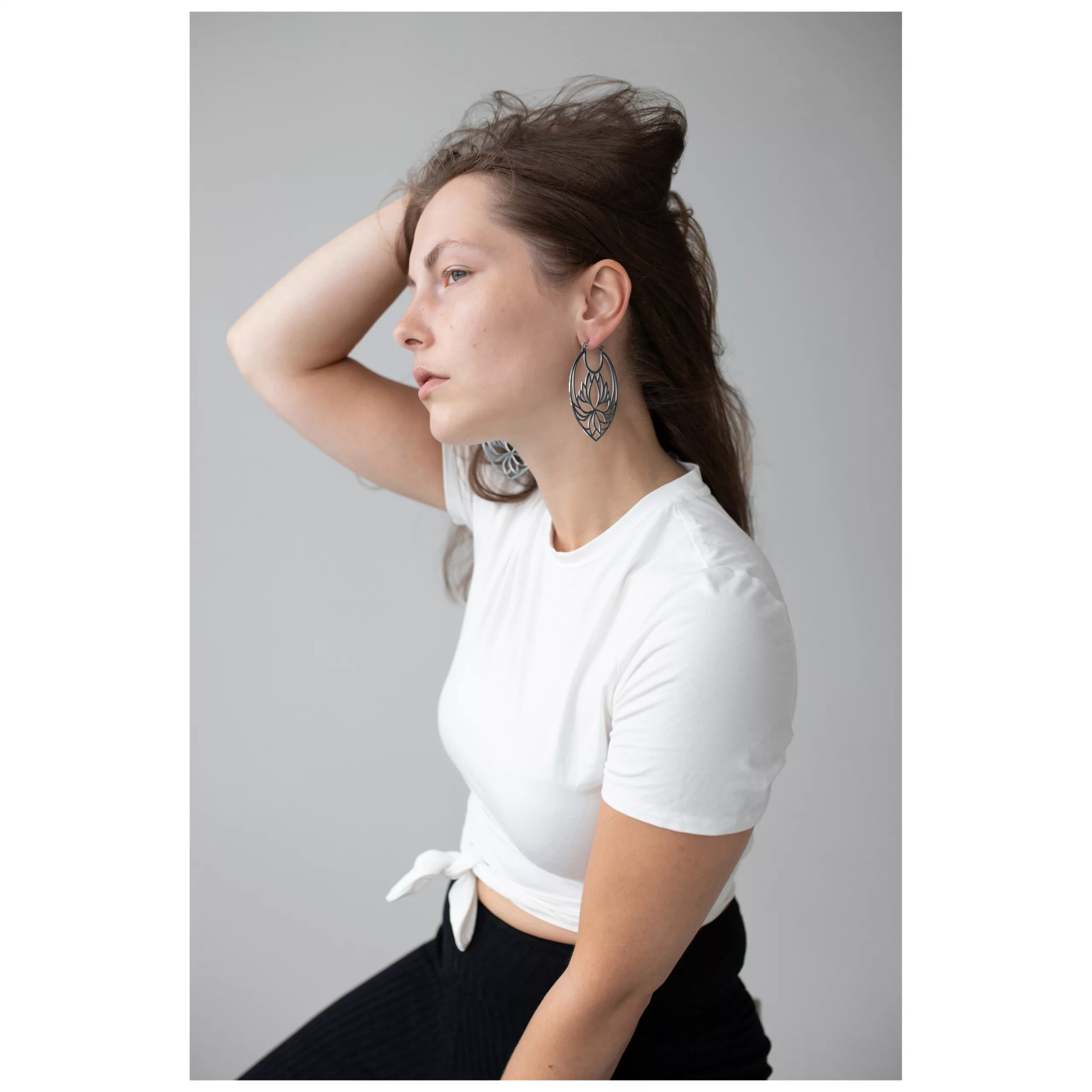 Lotus Hoops Ohrringe in Schwarz und Silber Frau mit Lotus Hoops Ohrringen aus Edelstahl in Schwarz und Silber auf grauem Hintergrund