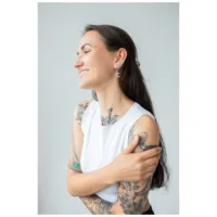 Silberfarbene Little Moonchild Creolen am Ohr Frau mit tätowierten Armen trägt silberfarbene Little Moonchild Creolen