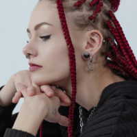 Silberne Little Ball Closure Hoops im Ohr getragen Frau mit roten Dreadlocks trägt silberne Ohrringe und Nasenpiercings, seitliches Profil