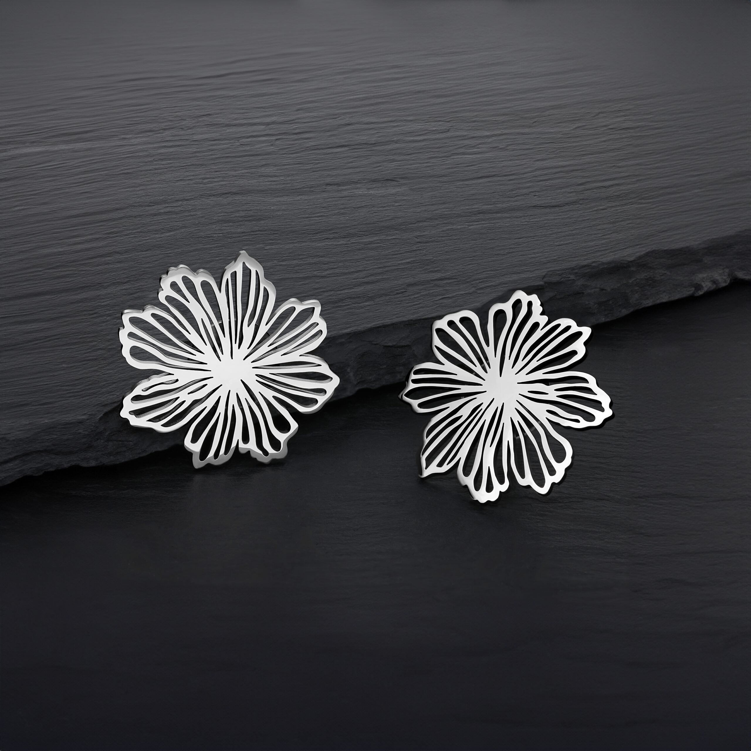 Feine Blumen Ohrstecker aus Edelstahl Zwei silberne Blumen Ohrstecker aus Edelstahl auf dunklem Hintergrund