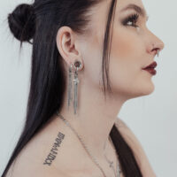 Silberne Little Shooting Star Hoops im Ohr Frau mit langen schwarzen Haaren trägt silberne Little Shooting Star Hoops und hat Tattoos am Hals.