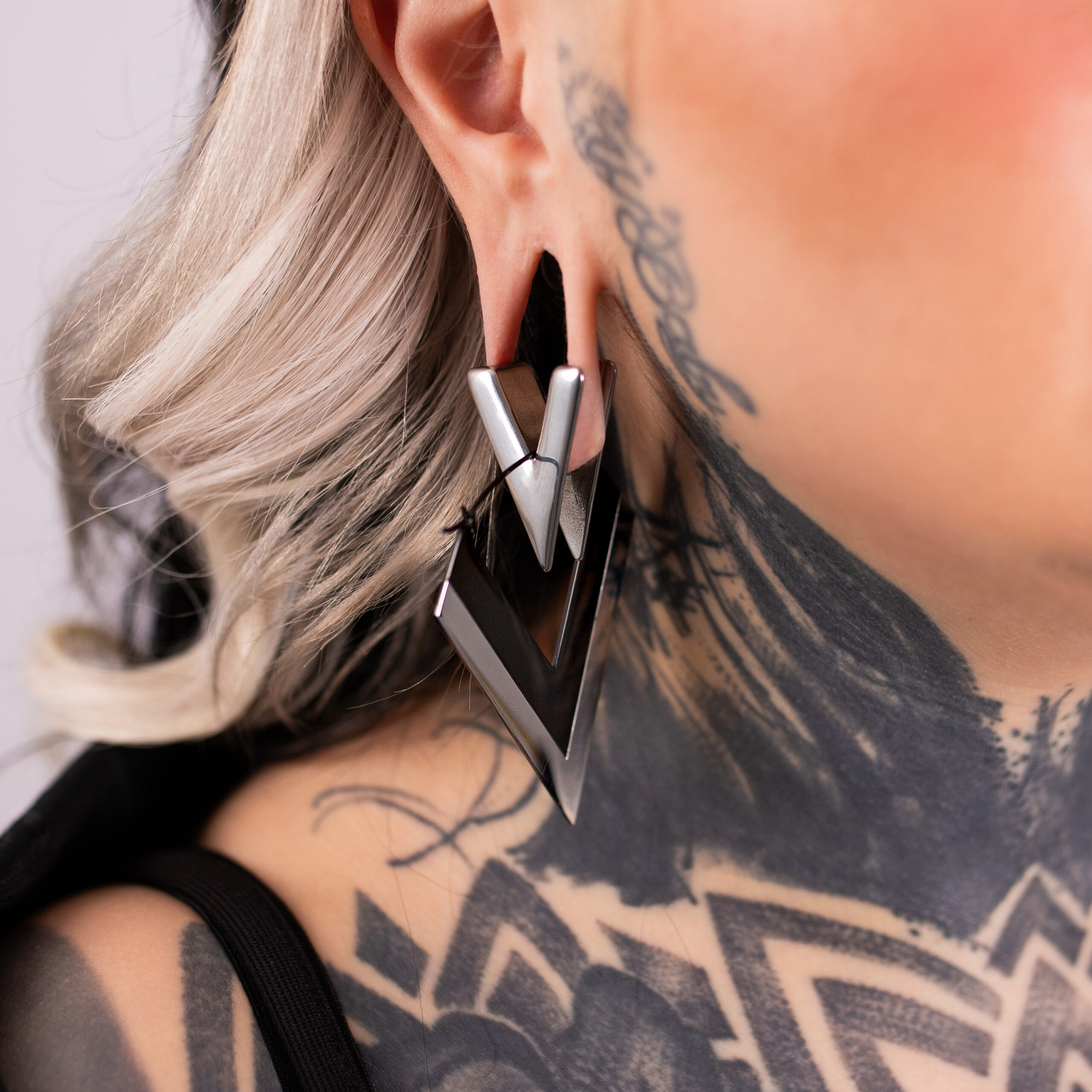 Verena Venus - Silberne und Schwarze V Hoops Silberne und schwarze V-förmige Ohrringe aus Chirurgenstahl an einem Ohr mit Tattoos