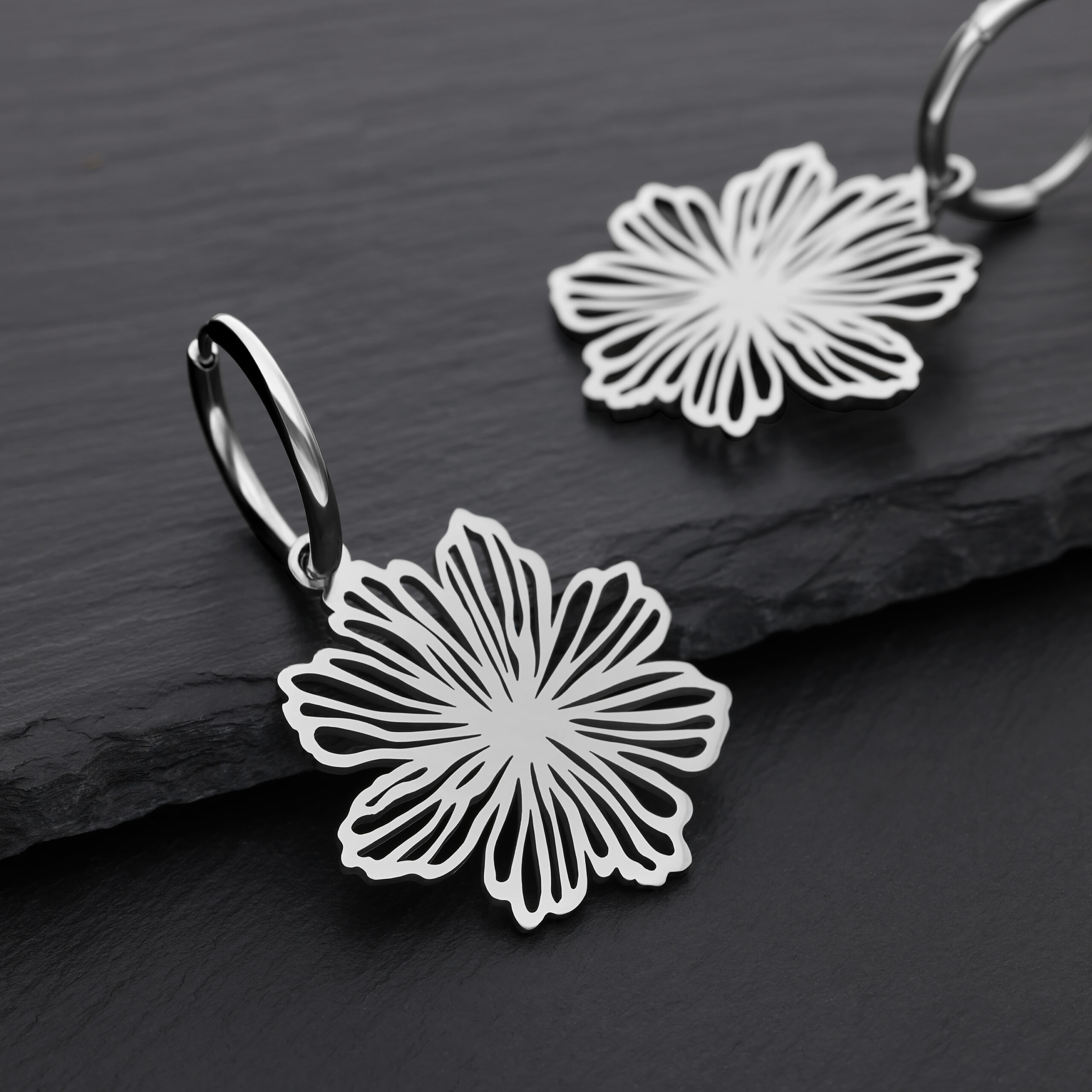 Zwei silberne Ohrringe mit Blumenmuster auf schwarzem Hintergrund