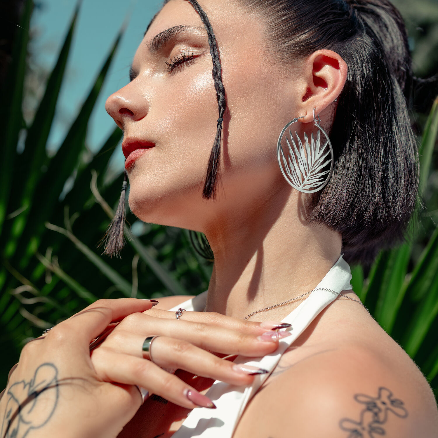 Noble Leaf Hoops in Silber und Schwarz Frau mit großen silbernen Ohrringen vor grüner Pflanze