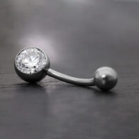 Elegantes Bauchnabelpiercing mit Kristall Schwarzes Bananabell aus Titan mit klarem Kristall auf grauem Hintergrund