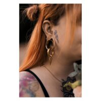 Frau mit rotem Haar trägt goldenen Monstera Push-Fit Labret im Ohr, Tattoos sichtbar