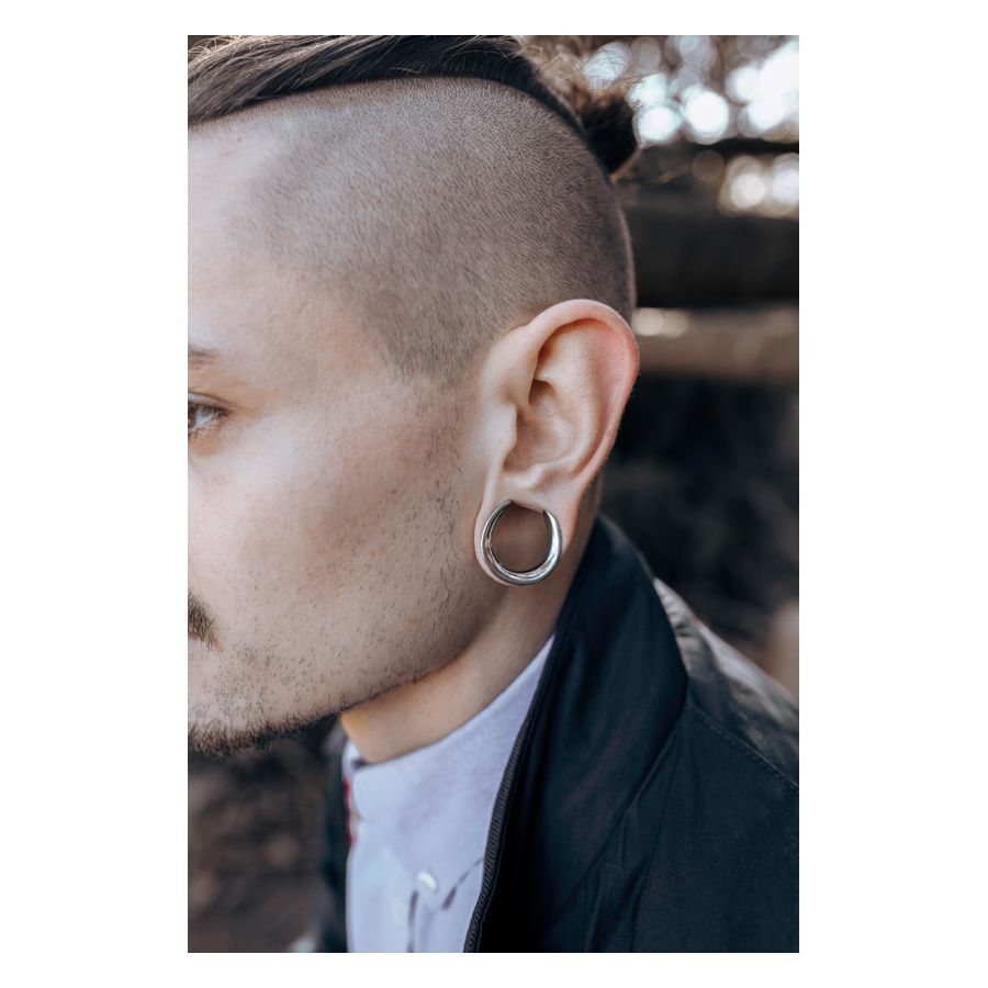 Stylische Ear Saddles aus Chirurgenstahl Mann mit silbernen Ear Saddles im Ohr vor unscharfem Hintergrund