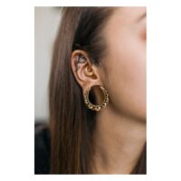 Blumen Ohrsättel in Gold am Ohr getragen Goldene Blumen Ohrsättel in Ohr mit weiteren Piercings auf neutralem Hintergrund