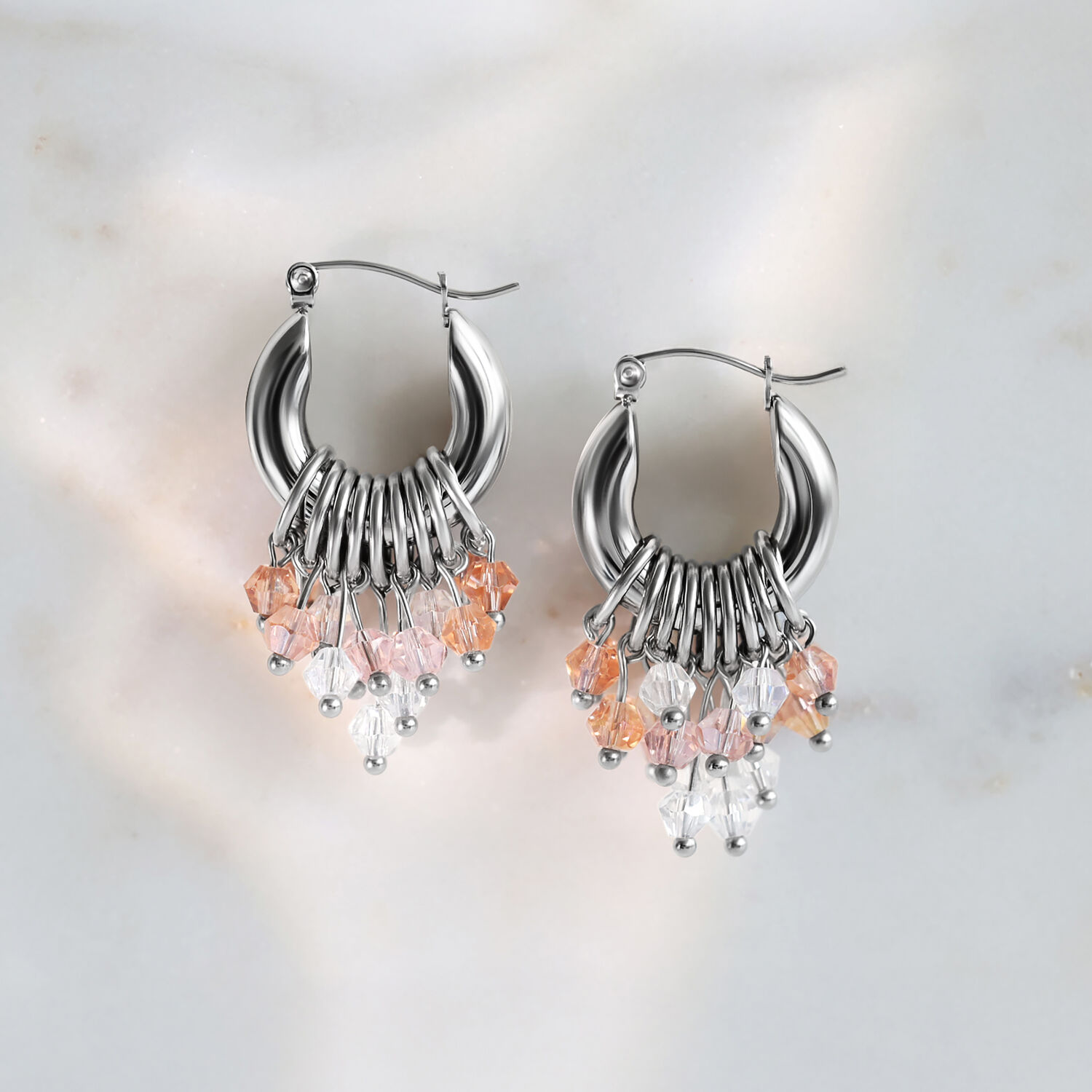 Silberfarbene Glamour Hoops mit Kristallen Silberne Ohrringe mit rosa und klaren Kristallen auf Marmorhintergrund