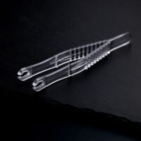Sterile Runde Piercingzangen auf schwarzem Hintergrund Zwei transparente, sterile Runde Piercingzangen liegen überkreuzt auf einem dunklen Hintergrund.